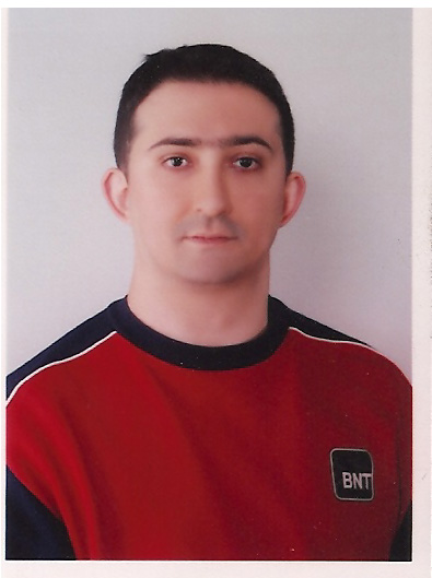 Oguz in Instanbul Turkey head shot of a dark haired young man with fair complexion looking straight at camera from white wall wearing a collarless shirt which looks a bit like a star trek costume